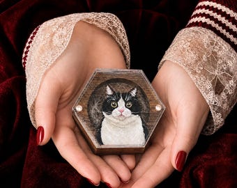 May include: A hexagonal wooden box featuring a detailed portrait of a black and white cat on the lid. The cat has large yellow eyes, a pink nose, and white fur on its chest and face, set against a dark wood background within a clear frame.