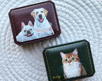 May include: Two rectangular jewelry boxes with hand-painted pet portraits. The burgundy box features a white French Bulldog and a yellow Labrador Retriever. The dark green box displays a brown and white cat with the name Holly written in gold script.