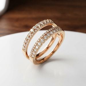 May include: A rose gold ring guard featuring two parallel bands connected at the base, each set with a row of small, round, clear white diamonds that catch the light, creating a sparkling, layered appearance for a ring set.