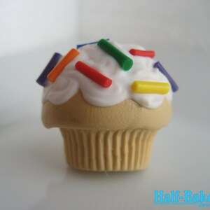 Könnte beinhalten: Ein weißer, mit Zuckerguss überzogener Cupcake mit bunten Streuseln, darunter rot, orange, gelb, grün und lila. Der Cupcake befindet sich auf einem weißen Hintergrund.