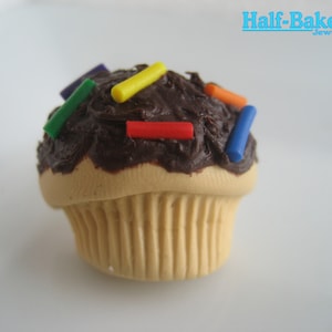 Könnte beinhalten: Ein Mini-Schokoladen-Cupcake mit braunem Frosting und bunten Streuseln. Der Cupcake ist aus Polymer Clay gefertigt und ein handgemachtes Stück.