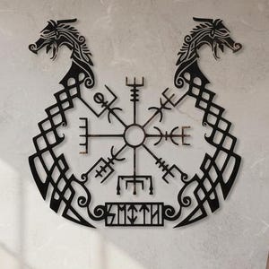 Peut inclure: Une décoration murale en métal noir représentant deux têtes de dragon symétriques tournées vers l'extérieur, reliées par des motifs de nœuds complexes. Au centre, un symbole de boussole Vegvisir est affiché avec le nom SMITH dans un cadre.