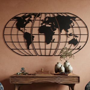 Op de afbeelding: Een zwarte metalen wereldkaart als wanddecoratie met een rasterontwerp, opgehangen boven een houten bureau. De kaart toont de continenten in silhouet tegen een reeks verticale en horizontale lijnen in een wereldbol-projectie.