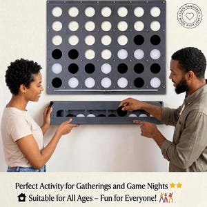 Könnte beinhalten: Ein großes, graues Connect-Four-Spielbrett mit schwarzen und weißen Spielsteinen. Das Spielbrett ist an einer weißen Wand befestigt, und zwei Personen interagieren mit dem Spiel. Der Text "100% Handmade, Made with Love" befindet sich oben rechts.