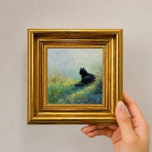 May include: A small square painting in a decorative gold frame featuring a black cat sitting in a field of tall green and yellow grass under a soft sky. The artwork depicts the cat in profile, looking toward the horizon amidst the textured landscape.