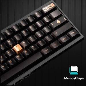 Puede incluir: Un teclado mecánico negro con teclas personalizadas y letras de color cobre. La fila superior incluye cuatro teclas especiales con símbolos de palos de cartas. La tecla J es de color cobre y la tecla de intro presenta un icono de pica.