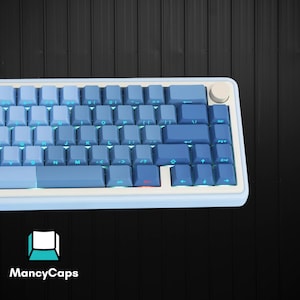 May include: A mechanical keyboard featuring a gradient of light to dark blue keycaps, a white frame, and a circular knob in the top right corner. The keys are backlit with a cyan glow, and the logo MancyCaps is visible in the bottom left corner.