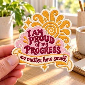 May include: An embroidered patch featuring a yellow sun, a pink cloud, and a cream-colored banner. The text reads: I AM PROUD of my PROGRESS no matter how small. The design uses dark red, yellow, pink, and cream thread colors.