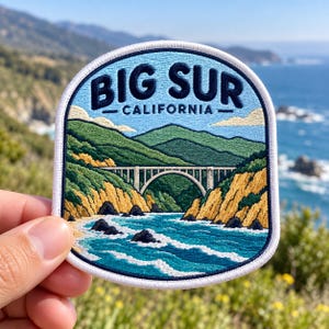 May include: A rounded rectangular embroidered patch featuring a landscape of Big Sur, California. The design includes a light blue sky, green hills, a tan arched bridge, and blue ocean waves crashing against yellow and green rocky cliffs.