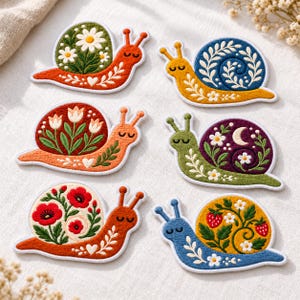 May include: Six embroidered snail patches featuring diverse designs. One has a green shell with white daisies, one a blue shell with white vines, one a red shell with tulips, one a purple shell with a moon, one a cream shell with red poppies, and one a yellow shell with strawberries.