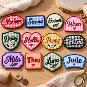 May include: A collection of twelve embroidered fabric patches in various shapes and colors, each featuring a unique name stitched in cursive or print. The patches display patterns like gingham, stripes, and solid colors, accented with small embroidered motifs such as flowers, hearts, and stars.