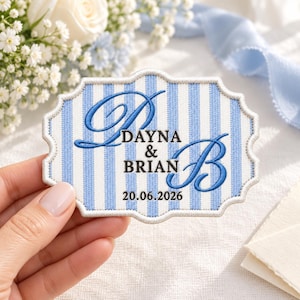 May include: A scalloped-edge embroidered patch featuring a light blue and white vertical striped pattern. The patch displays the blue embroidered initials D and B, the names DAYNA & BRIAN, and the date 20.06.2026 in dark lettering.