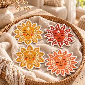 May include: Four embroidered sun-shaped patches featuring closed eyes, smiling mouths, and rosy cheeks. Two patches are yellow with white borders, and two are orange-red with white borders, all displaying intricate leaf-like ray details.