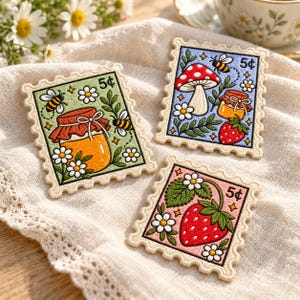May include: Three rectangular embroidered patches shaped like postage stamps. One features a honey jar with bees and daisies on green, one a mushroom and strawberry on blue, and one a strawberry with daisies on pink. Each displays a 5¢ label.