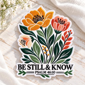 May include: An embroidered patch featuring a bouquet of yellow, coral, and cream flowers with dark green leaves and stems. The text "BE STILL & KNOW" and "PSALM 46:10" is stitched in black at the bottom, framed by a white border.