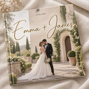 May include: A square photo album cover featuring a wedding photograph of a couple standing in front of a stone archway. The text "Emma + James" is printed in gold script, with the date "14.06.2026" centred above the names in a simple font.