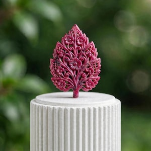 Può includere: Un intaglio a forma di foglia color magenta intenso con intricati motivi floreali traforati e delicati dettagli a griglia. Il pezzo è montato verticalmente su un piedistallo cilindrico bianco con una texture a coste verticali.