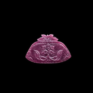 Puede incluir: Una piedra preciosa de color magenta intenso tallada con la forma de un pequeño monedero o bolsa. La superficie presenta un intrincado patrón floral en relieve con motivos simétricos de hojas y un diseño de flor central en la parte frontal.