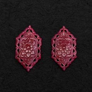 Puede incluir: Dos colgantes a juego de color rojo intenso en forma de diamante, con un intrincado patrón floral tallado en el centro. Cada pieza tiene un borde decorativo de filigrana calada que rodea el motivo floral central, creando un diseño simétrico.