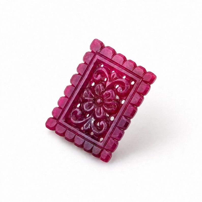 Op de afbeelding: Een rechthoekig, diep magentakleurig edelsteensnijwerk met een ingewikkeld, verhoogd bloemmotief in het midden. Het stuk is omlijst door een geschulpte, ingekeepte rand, wat gedetailleerd vakmanschap en een gepolijste afwerking laat zien.