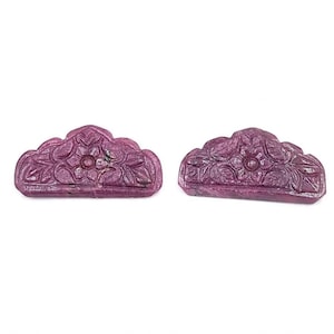 Pode incluir: Duas peças de pedra preciosa esculpidas em forma de semicírculo, de cor magenta profunda. Cada peça apresenta um motivo floral central com padrões de folhas circundantes, exibindo uma superfície esculpida em relevo com acabamento polido.