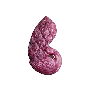 Puede incluir: Una talla de piedra preciosa de color magenta intenso con forma de ave con la cabeza inclinada hacia el cuerpo. La superficie presenta intrincados patrones de plumas grabados en las alas y el cuerpo, creando una apariencia texturizada y en capas.