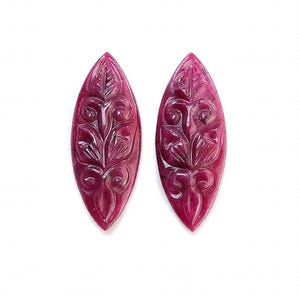 May include: Two marquise-shaped, deep magenta-coloured gemstones featuring intricate, hand-carved floral and scrollwork patterns across their surfaces. These polished, elongated cabochons display a rich, saturated hue with subtle variations in tone.