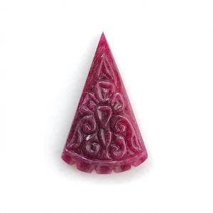 Puede incluir: Una talla de piedra preciosa de color magenta intenso con forma triangular que presenta un intrincado patrón de relieve de inspiración floral en su superficie frontal. La pieza tiene una parte superior puntiaguda y una base curva festoneada.