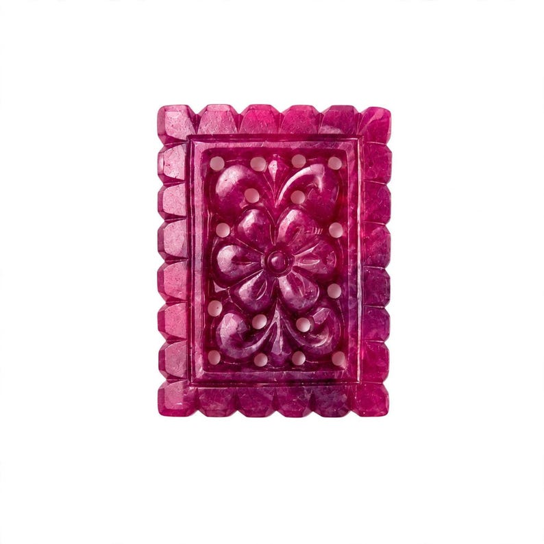 Op de afbeelding: Een rechthoekig, diep magentakleurig edelsteensnijwerk met een centraal bloemmotief met zes bloemblaadjes. Het stuk heeft een geschulpte, ingekeepte rand en ingewikkelde uitgesneden details rondom de bloem, wat een decoratief opengewerkt ontwerp cre&euml;ert.