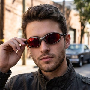 May include: A pair of sunglasses with a metallic silver frame and dark red, reflective lenses. The eyewear features a wrap-around design with thin, curved temples and a bridge that connects the two oval-shaped lenses, providing a sleek look.