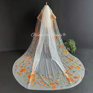 May include: A long, sheer white wedding veil featuring a hand-painted pattern of vibrant orange, yellow, and green autumn leaves scattered across the fabric. The text RoninArtGoods is printed in white script across the center of the veil.