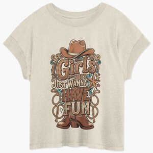 Könnte beinhalten: Hellbeige T-Shirt mit einem Grafikdesign. Das Design zeigt einen Cowboyhut, Stiefel und den Schriftzug "Girls Just Wanna Have Fun". Die Grafik hat einen Vintage-Stil mit Seil- und Sterndetails.