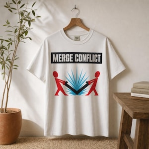 Puede incluir: Camiseta de color crema con la frase "MERGE CONFLICT" en un rectángulo negro. Debajo, dos figuras rojas tiran de un objeto negro con formas puntiagudas azules en el centro. La camiseta está colgada de una percha de madera.