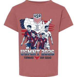 以下が含まれることがあります： ダスティローズ色の半袖Tシャツ。USAジャージを着た4人のサッカー選手、アメリカ合衆国の地図、USAの紋章、そして「USMNT 2026 FORWARD OUR SQUAD」という文字とロサンゼルスやダラスなどの都市名が記載されたグラフィックがプリントされています。