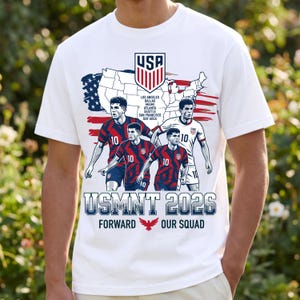以下が含まれることがあります： USAの地図、サッカーのUSAエンブレム、背番号10の赤と白のユニフォームを着た4人のサッカー選手が描かれた白いTシャツ。USA、都市名、USMNT 2026、赤い鷲のアイコンと共にFORWARD OUR SQUADという文字がプリントされています。