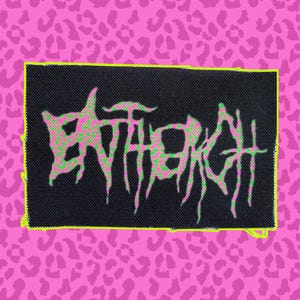 Puede incluir: Un parche rectangular negro con la palabra "ENTHROH" en una fuente verde y rosa desgastada. El parche tiene un borde amarillo neón y está sobre un fondo rosa con estampado de leopardo.