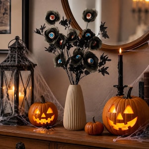 May include: A bouquet of black artificial flowers with realistic human eyeballs at their centers, arranged in a tall, ribbed, beige ceramic vase. The flowers feature varied iris colors including blue, brown, and orange, set against dark stems.