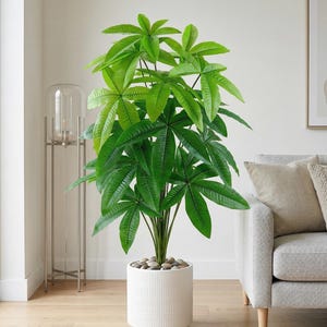 May include: A tall artificial money tree plant with vibrant green, palm-like leaves arranged in clusters. The plant is housed in a cylindrical white ceramic pot with a vertical ribbed texture, filled with smooth grey decorative river stones.