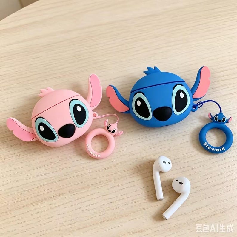 May include: Two silicone earphone cases shaped like cartoon characters, one in light pink and one in blue, each featuring large eyes and side ears. Both cases include a matching circular ring charm with a small character head and the text Steward.