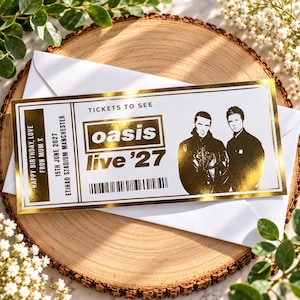 Könnte beinhalten: Ein rechteckiges Souvenir-Ticket mit Goldfolien-Akzenten, das den Text TICKETS TO SEE oasis live '27, 15TH JUNE 2027, ETIHAD STADIUM MANCHESTER und HAPPY BIRTHDAY, LOVE FROM MUM X sowie eine schwarz-weiße Grafik von zwei Personen zeigt.