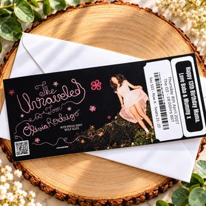 May include: A black rectangular concert ticket featuring pink cursive text reading The Unraveled Tour Olivia Rodrigo with special guest Wolf Alice. It includes a photo of a person in a light pink dress, a barcode, a QR code, and event details.