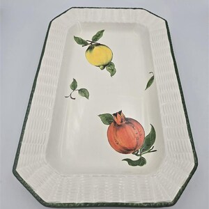 May include: A rectangular ceramic serving platter with a cream-colored base and a textured basket-weave border in white. The center features hand-painted illustrations of a yellow lemon and a red pomegranate with green leaves on a white background.