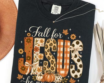 Könnte beinhalten: Ein schwarzes T-Shirt mit Rundhalsausschnitt und dem Text Fall for JESUS he never leaves. Die Buchstaben sind mit orangefarbenen Blumen-, Leoparden-, Karomustern und Punkten gefüllt, verziert mit kleinen Schleifen und Kürbisbildern.