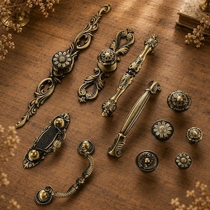 May include: An assortment of antique brass cabinet hardware, including handles and knobs. The hardware features ornate floral and scrollwork designs. The pieces are arranged on a wooden surface, showcasing their intricate details and aged finish.