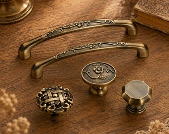 May include: A collection of five antique brass hardware pieces including two arched drawer pulls with floral engravings, one round knob with a central flower design, one round knob with a woven lattice pattern, and one octagonal knob.