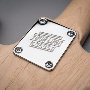 以下が含まれることがあります： ギターのネックジョイントのクローズアップ。銀色の金属プレートに「YOUR LOGO HERE」の文字が刻まれています。4本のネジで、ギターボディの明るい色の木材にプレートが固定されています。