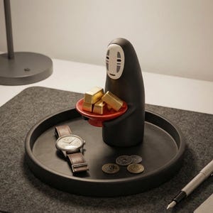 May include: A black decorative figure holding a red plate with gold bars, placed on a black tray. A wristwatch with a brown leather band and several coins are also on the tray. A pen is on the right.