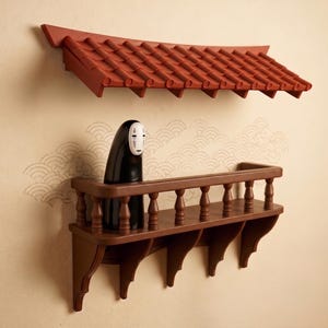 Może przedstawiać: Montowana na ścianie brązowa drewniana półka z balustradą oraz oddzielny daszek z czerwonych dachówek powyżej. Czarno-biała figurka z gładką, zaokrągloną głową i maskowatą twarzą stoi na półce, która posiada ozdobne wsporniki montażowe.