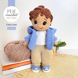 May include: A crochet doll with brown hair, wearing a white shirt, a light blue hooded jacket, tan pants, and blue and white sneakers. The text on the image reads PDF crochet pattern, English, 8 inches (20 cm). The doll is 8 inches tall.