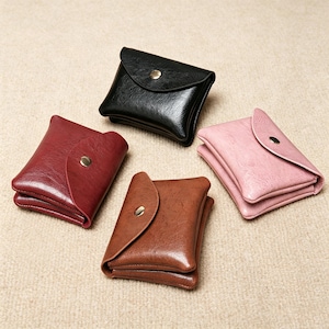 Puede incluir: Cuatro carteras pequeñas y rectangulares con un acabado de piel sintética texturizada. Cada cartera cuenta con una solapa redondeada asegurada por un botón de presión de metal dorado. Los colores disponibles son negro, rojo oscuro, marrón y rosa.